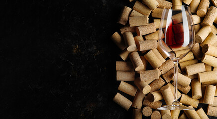 A glass of red wine and a lot of wine bottle caps on a black background. There are no people in the photo. There is an empty space to insert. Winery, restaurant, wine collection.