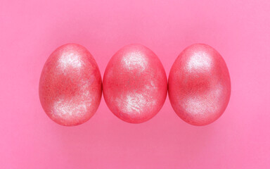 Three 3 Easter eggs colored in pink shiny color on pink paper background. Glitter paint for eggs. Greetings card for easter holiday. Place for text.