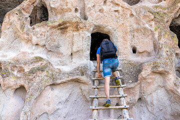 Obraz premium Man climbing up ladder on Main Loop trail in Bandelier National Monument in New Mexico during summer on canyon cliff to cave dwelling used by native people