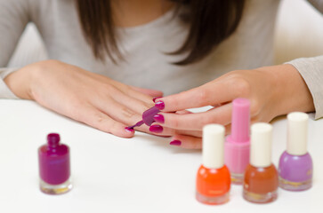 Obraz na płótnie Canvas Young woman painting nails using purple nail varnish at home.