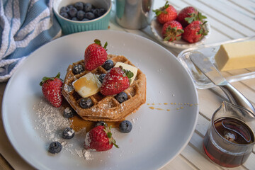 Begian waffles with fresh blueberries,strawberries butter. and pure maple syrup on a white natural wood table top view