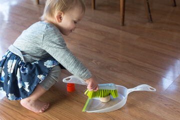 20 month old toddler practices sweeping using a dustpan and brush to move toys around; learning...