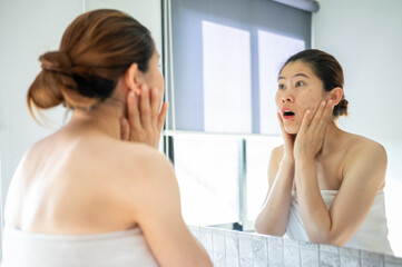 Obraz na płótnie Canvas Asian woman feeling stress after looking her face in mirror. She dissatisfied her face caused of acne and scar problem.