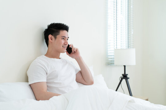 Asian handsome man talk on mobile phone call on bed at home in morning. - Powered by Adobe
