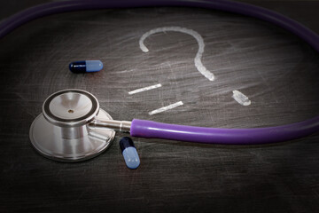 medicine, concept, stethoscope and pills on a black board, chalk a question mark