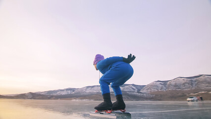 The child train on ice speed skating. The athlete at the start, in a sports stance. The kid girl skates in the winter in sportswear, sport glasses. Children speed skating short long track. Outdoor.