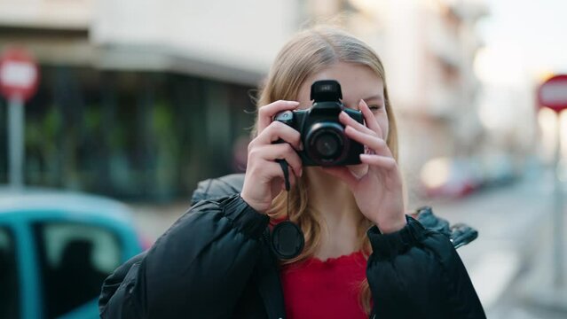 Young blonde girl smiling confident using professional camera at street