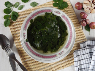 Moringa clear soup or sayur bening daun kelor is Indonesian traditional daily menu, made from moringa oleifera folium leaves seasoning with shallot, lemon grass, and salt. Focus selection.