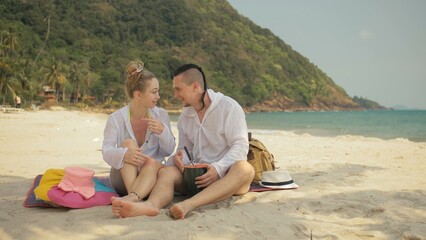 The cheerful love couple holding and eating slices of watermelon on tropical sand beach sea. Romantic lovers two people caucasian spend summer weekend in outdoor. Hat, backpack white shirt beachwear.