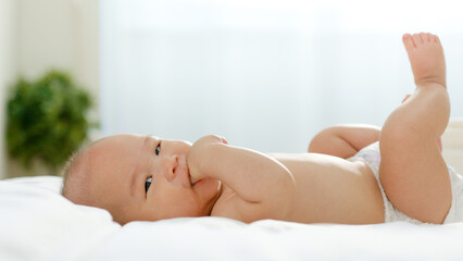 Asian newborn baby sucking his fingers on bed