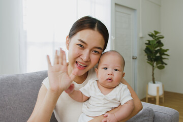 Point of view, Young Asian mother and her newborn baby smiling and say hello / goodbye via video...