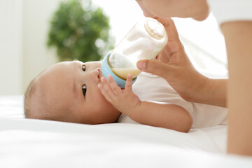 Mother feeding milk to Asian newborn baby on white bed