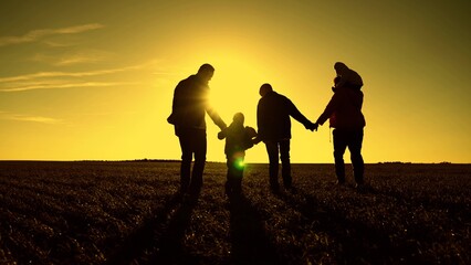 Silhouette of happy family, mom children dad walk through green grass holding hands. Happy family walk at sunset. Dad, mom, kids sons are walking in park in sun. Family walks, childhood dreams.