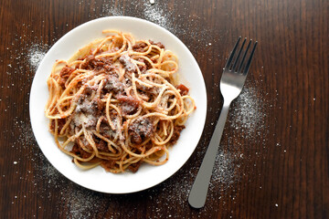 Spaghetti Bolognese with minced beef, onion, chopped tomato, garlic, olive oil, stock cube, tomato puree and Italian herb. Traditional Italian food in white plate with a fork. Flat lay top view photo.