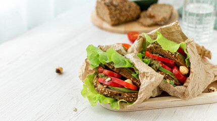 Vegan sandwiches of whole grain bread, tomatoes, peppers and avocados with spicy sauce and lettuce leaves wrapped in paper on a wooden tray. Close-up. Healthy food. Diet breakfast.