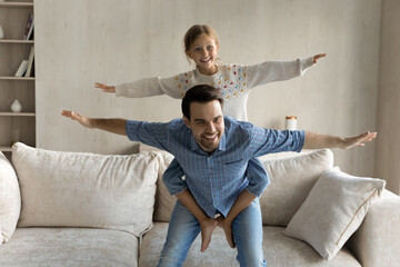 Excited dad piggybacking happy laughing little daughter girl with flying arms, playing airplane...