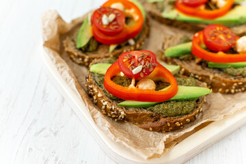 Vegan sandwiches with rye bread and vegetables on a wooden tray on a white table. A healthy breakfast or snack. Side view. Space for text. Close-up. Dietary nutrition.
