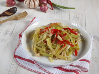 Stir fry or sauteed chayote squash or tumis labu siam is Indonesian daily dish. Simple and easy to cook. Served in white plate on white wooden table with some ingredients. 