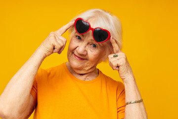 smiling elderly woman in casual t-shirt sunglasses yellow background