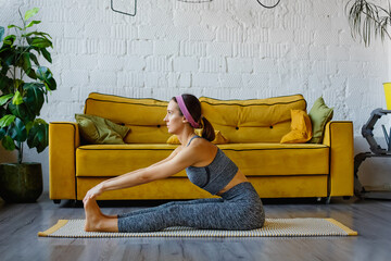 A sporty young woman doing morning exercises alone in the living room by the yellow sofa, a serious...