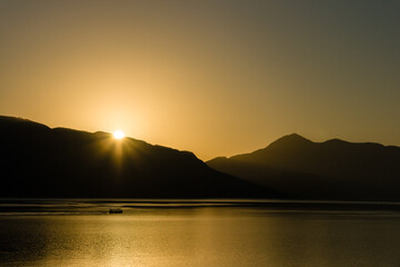 Sunrise at the sea with a boat in the water - The sun rises behind hills