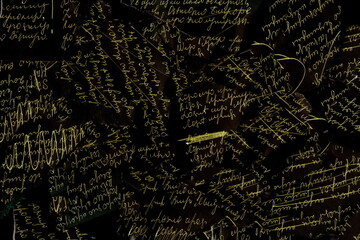 The texture of unreadable handwriting on scraps of paper on a black background. A torn letter in a black background.
