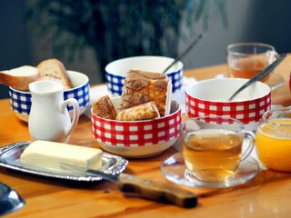 Everyday diet breakfast with butter, milk noodles in checkered tureens and tea with honey on the kitchen table. Side view.
