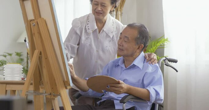 Senior man painting picture at living room. He sitting on wheelchair while painting pictures.