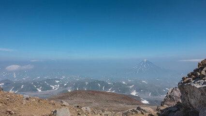 View from the top of the mountain to the Kamchatka valley. Snow-covered hills and the conical stratovolcano Vilyuchinsky are visible far below. Blue sky. Сopy space.