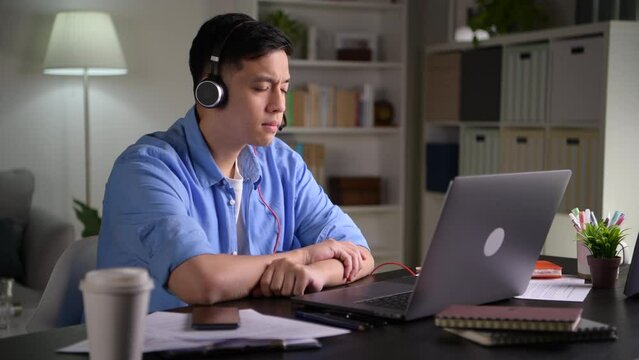 Focused young Asian business person, entrepreneur, speaker, student, office worker wearing headphones, looking at laptop screen and speaking in video conference call, giving lecture, joining online
