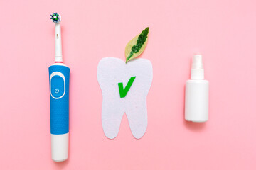 Hygiene of the oral cavity. An electric toothbrush, a breath freshener, and a felt-cut tooth with a leaf. Flat lay. Pink background