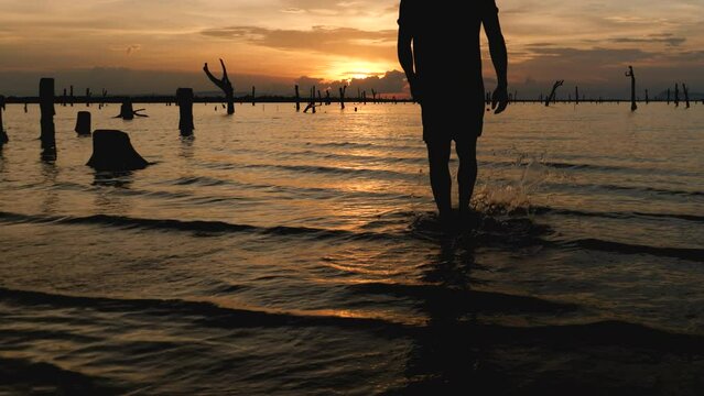 Slow Motion, Silhouette of young man walking into the lake during sunset with hands raised, awareness of success