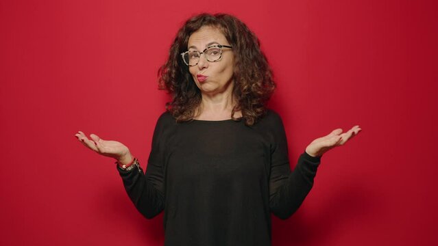 Middle age woman with doubt gesture standing over red background
