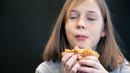 A little girl with freckles eats a burger.