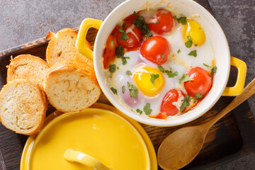Portioned baked eggs in ceramic cocotte on white wooden table, breakfast closeup in the wooden tray...
