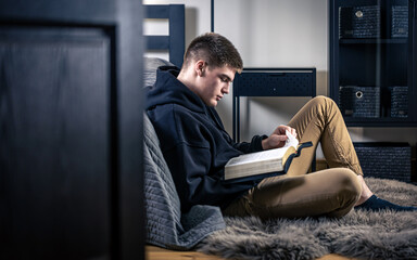 A young man sits in a room and reads the Bible.