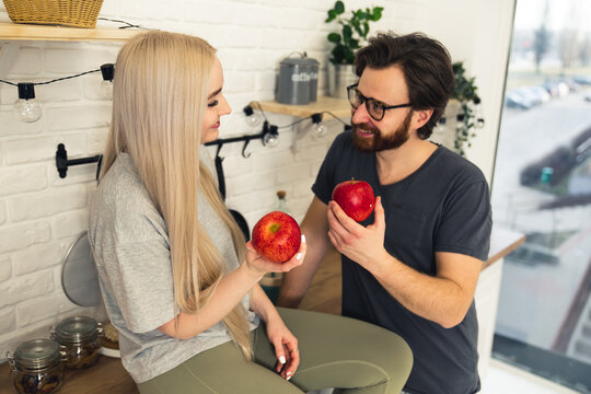 cute couple in their apartment sharing good habits and eating one apple a day, promoting healthy eating while sitting in their modern kitchen. High quality photo - Powered by Adobe