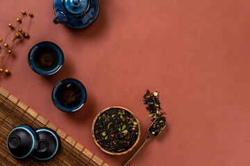 Blue teapot, cup of tea and tea leaves on brown background. Hot herbal tea is in the teapot on the table. Copy space.