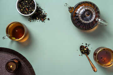 Glass teapot, cup of tea and tea leaves on green background. Hot herbal tea is in the glass teapot on the table. Copy space. © Svetlana 