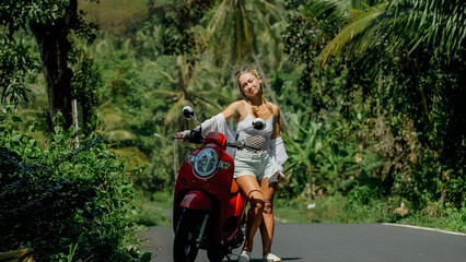 Woman on red scooter in white clothes drive on forest road trail. Dancing trip. One girl caucasian tourist in sunglasses dance, relax, rest near motorbike. Asia Thailand ride tourism. Motorcycle rent.