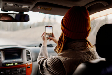 a girl in a hat in a car with a phone takes pictures of nature