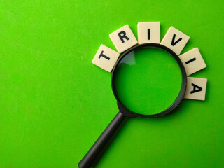 Top view magnifying glass and word toys with text TRIVIA on a green background.
