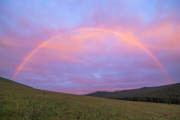 Beautiful scene of a Beautiful full rainbow stretches across a valley at sunset © Abfeig/Wirestock