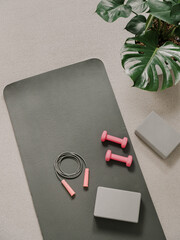 Stylish gray and pink home fitness flat lay. Top view of gray sport mat, yoga block, skipping rope...