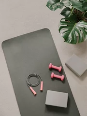 Wandcirkels Yogaschool Stylish gray and pink home fitness flat lay. Top view of gray sport mat, yoga block, skipping rope and pink dumbbells on neutral carpet background, monstera plant. Set for pilates, fitness, yoga  © fascinadora