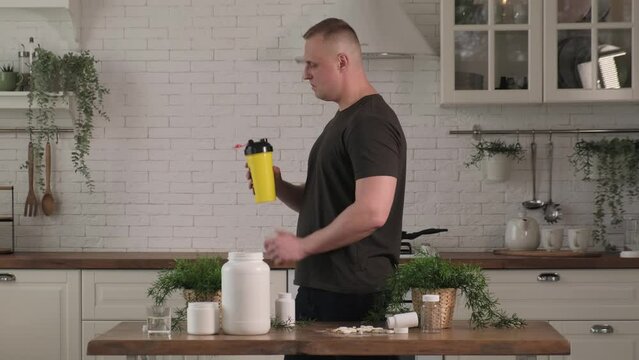 Man drinking protein shake in the kitchen from a shaker. Concept: sports supplements, nutrition, bodybuilding, fitness
