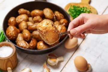 a woman's hand takes fried potatoes from a frying pan, next to other natural products - garlic and green onions, farm eggs and salt, whole cooked food in a rustic style