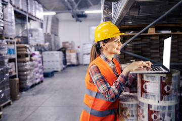 A smiling female warehouse employee working on laptop.