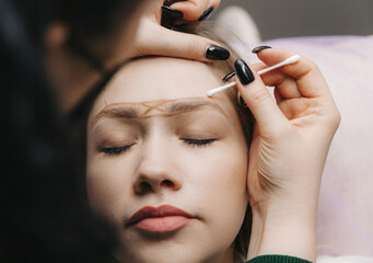 girl with permanent makeup on her eyebrows. The makeup artist makes markings with a brown pencil...