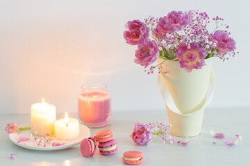 bouquet of pink spring flowers and burning candles on  white table